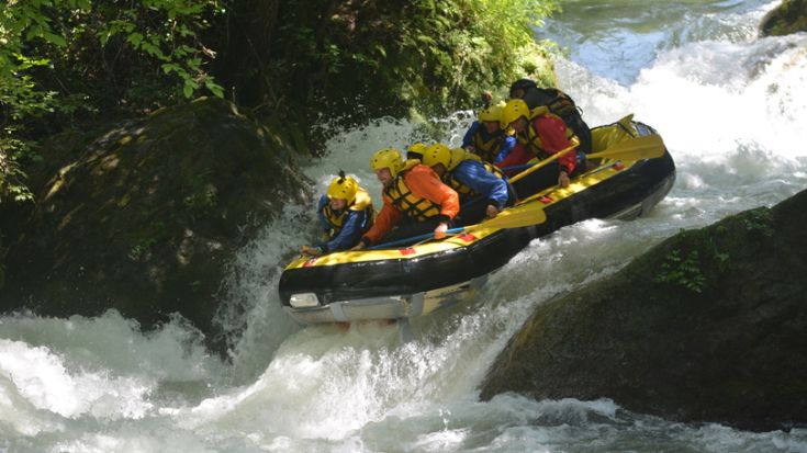 Un gruppo di persone pratica rafting su un fiume con rapide intense, circondati da una natura selvaggia.
