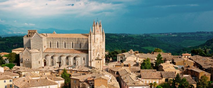 Panorama della cattedrale di Orvieto, circondata da colline e alberi verdi.