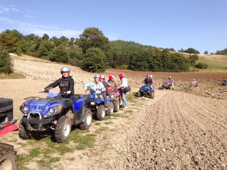 Un gruppo di persone partecipa a un'escursione in quad in un paesaggio naturale collinare.