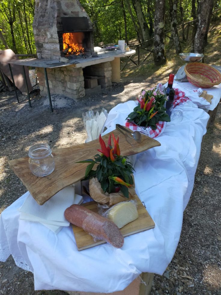 Un tavolo allestito per un pranzo all'aperto, con cibi freschi e un barbecue acceso.