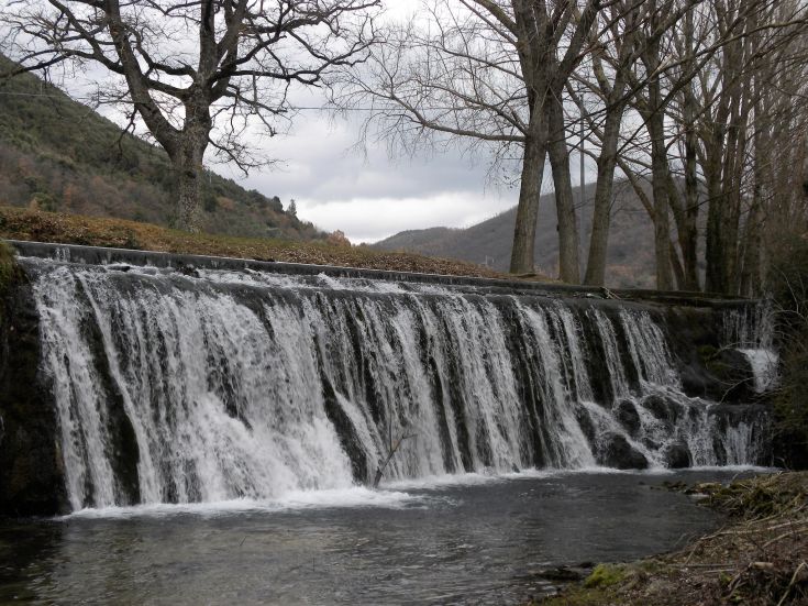 Una cascata immersa in un paesaggio naturale, circondata da alberi e montagne, ideale per momenti sereni.