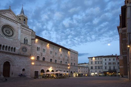 Panorama di una piazza in Umbria al crepuscolo, con un cielo sereno e luci soffuse che creano un'atmosfera accogliente.