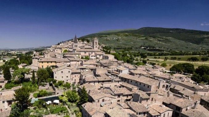 Un panorama di una tranquilla città medievale umbra, circondata da colline verdi.