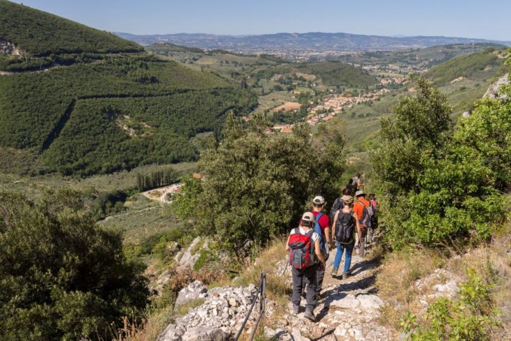 Un gruppo di escursionisti cammina lungo un sentiero immerso nella natura, circondato da colline verdi e un cielo sereno.