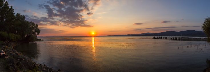 Un tramonto si riflette tranquillamente sull'acqua del lago, creando un'atmosfera calma e rilassante.