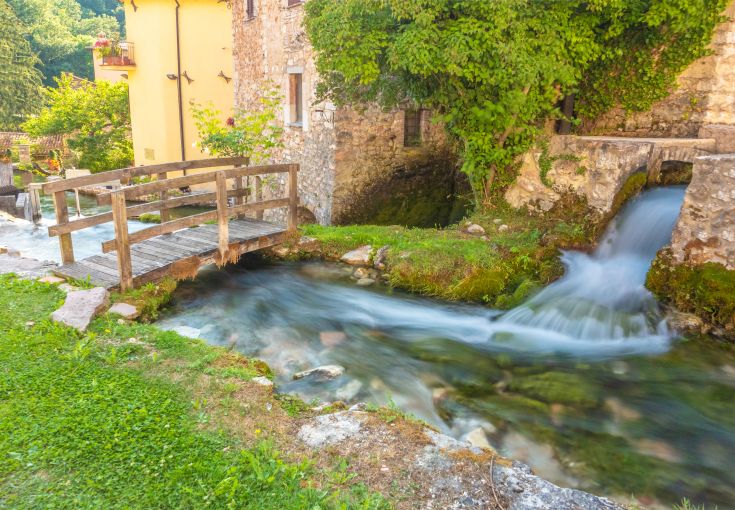 Una scena di un ponte in legno su un ruscello, immerso nella vegetazione tipica della campagna umbra.