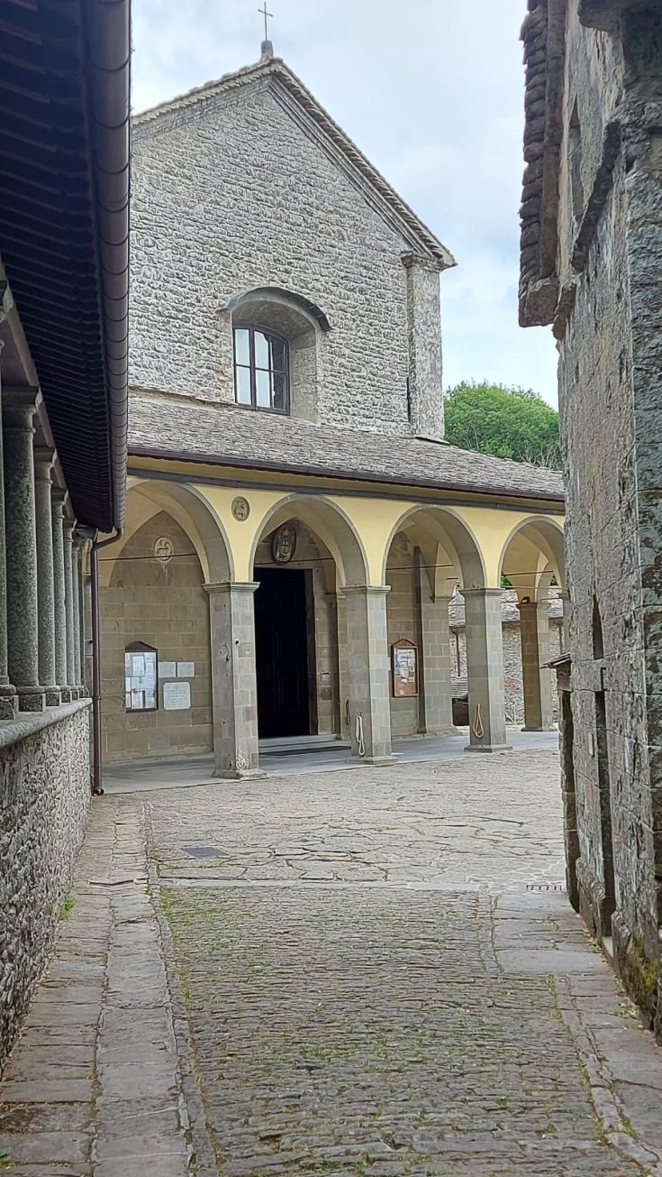 Una chiesa in pietra si trova sopra un cortile, mostrando archi e dettagli architettonici.