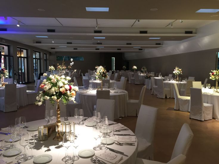 Sala da pranzo sobria, allestita per un evento, con semplici decorazioni floreali e tovaglie bianche.