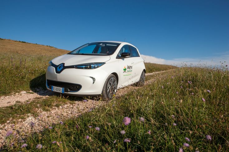 Un'auto elettrica Renault su una strada in pietra circondata da natura, simbolo di un turismo sostenibile.