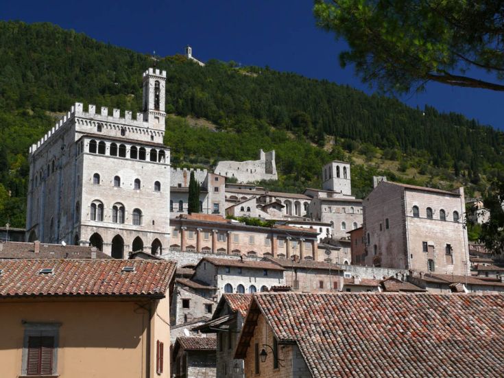Una scena che ritrae il palazzo dei Consoli di Gubbio su una collina verde, circondato da vegetazione.