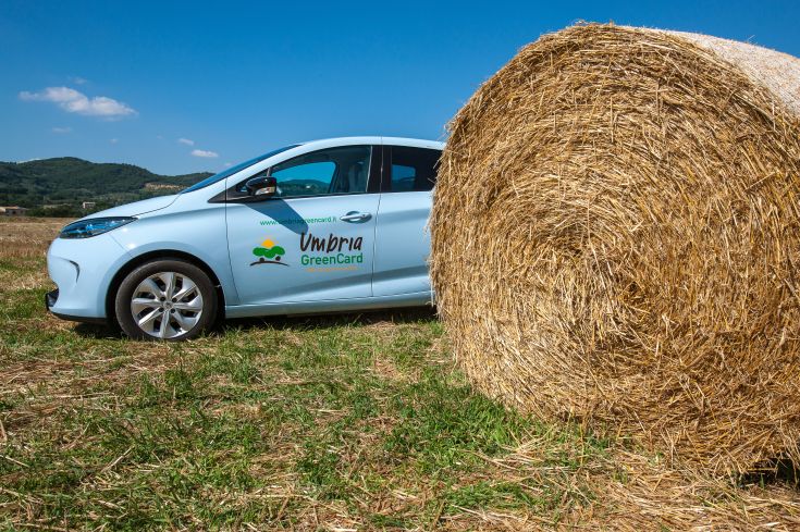 Un'auto elettrica parcheggiata in un campo dell'Umbria, rappresenta un approccio sostenibile alla mobilità.