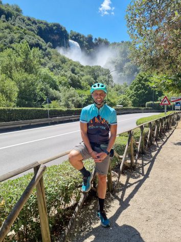 Un ciclista sorride davanti a una cascata, immerso nella natura umbra.