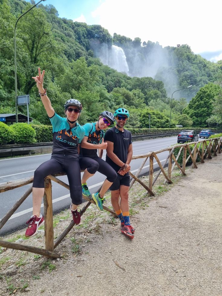 Un gruppo di ciclisti esplora la natura in Umbria, con una cascata visibile sullo sfondo.