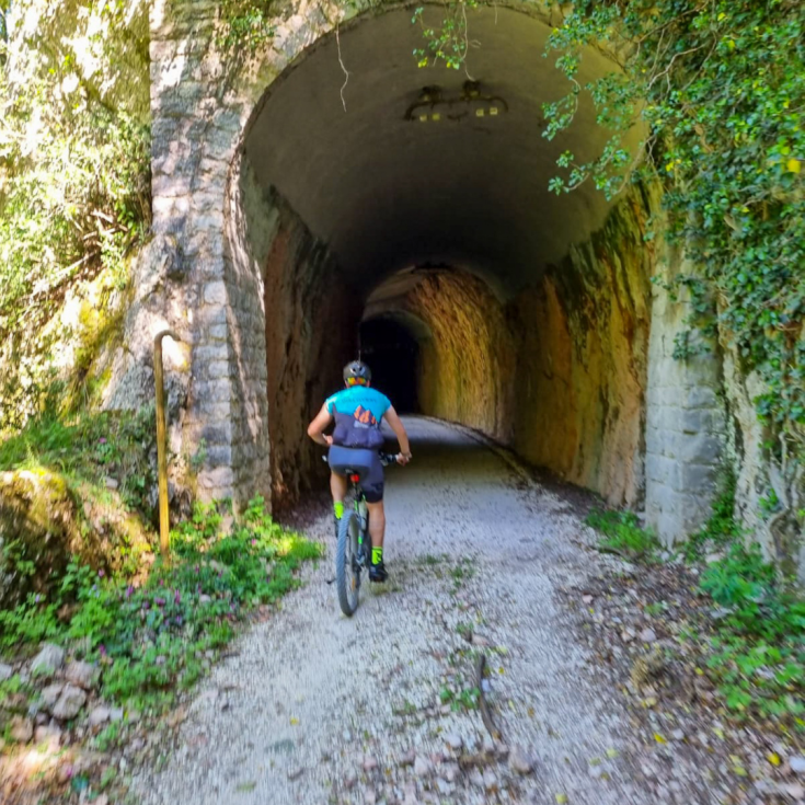 Un ciclista attraversa una galleria circondata dalla natura, su l' ex ferrovia Spoleto - Norcia 
