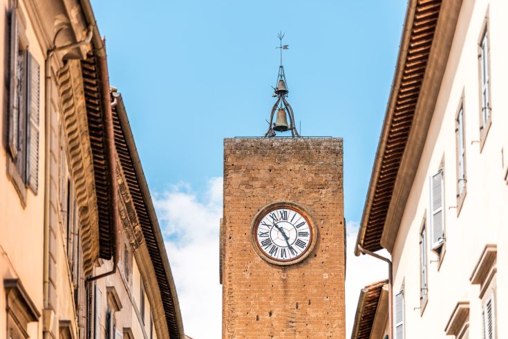 Una torre con orologio si erge tra palazzi storici, delineando un paesaggio urbano caratteristico.