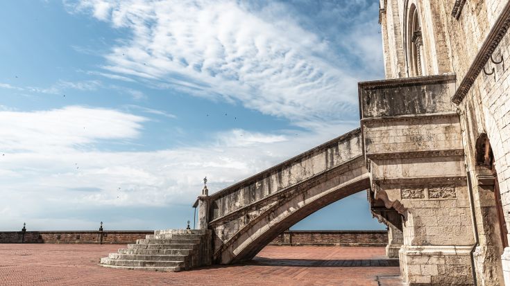 Una scala che conduce al palazzo dei Consoli di Gubbio, sotto un cielo blu con alcune nuvole.
