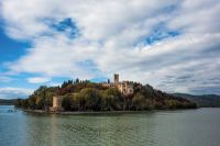 Un palazzo si erge su un'isola circondata da un lago tranquillo e un cielo coperto di nuvole.
