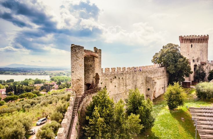 Panorama di un castello storico immerso nella natura, con un lago che si estende sullo sfondo.