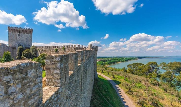 Un castello si trova di fronte a un lago azzurro, circondato da un cielo sereno e nuvole leggere.