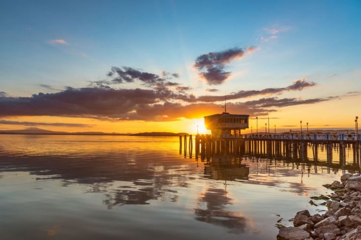 Un elegante tramonto riflesso sull'acqua, accompagnato da un palazzo in legno e nuvole dai colori vivaci.