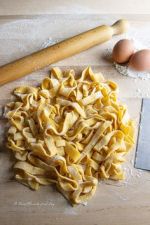 Tagliatelle fresche su un piano di lavoro con uova e farina, pronte per la cottura. Ottimo piatto della cucina italiana.