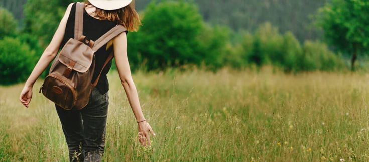 Una persona cammina in un campo con uno zaino. La natura circostante trasmette un gradevole senso di libertà.