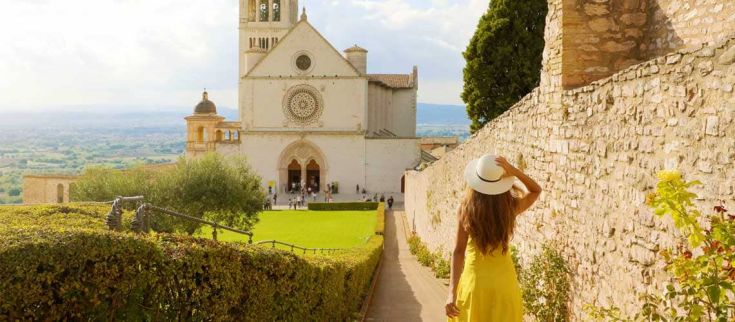 Una giovane donna con un cappello bianco e vestito giallo osserva la basilica di San Francesco in lontananza.