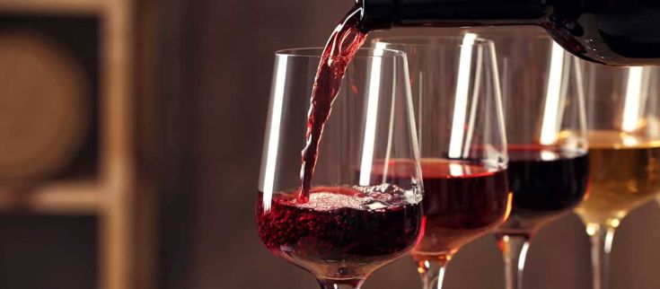 Un bicchiere di vino rosso viene versato in un insieme di calici, mostrando diverse tonalità di vino.