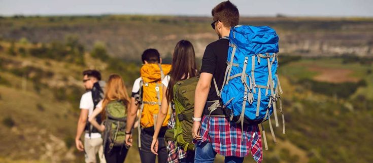 Un gruppo di escursionisti attraversa un paesaggio ampio, con zaini sulle spalle, circondati dalla natura.