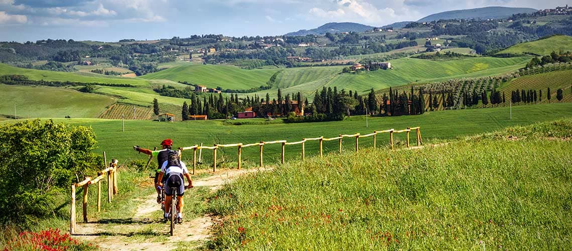 Un gruppo di ciclisti percorre una tranquilla strada circondata da un paesaggio collinare verde e rigoglioso.