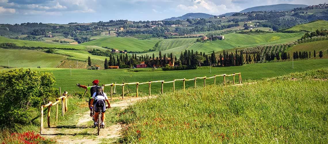 Un gruppo di ciclisti percorre una tranquilla strada circondata da un paesaggio collinare verde e rigoglioso.