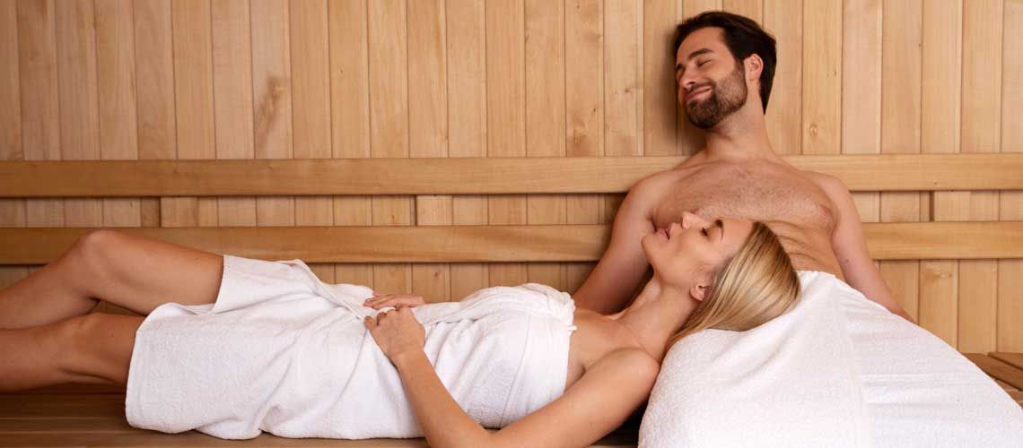Due persone si trovano all'interno di una sauna in legno, godendosi un attimo di tranquillità e benessere.