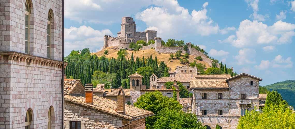 Un paesaggio umbro con una fortezza antica e case in pietra, circondato da vegetazione verde.