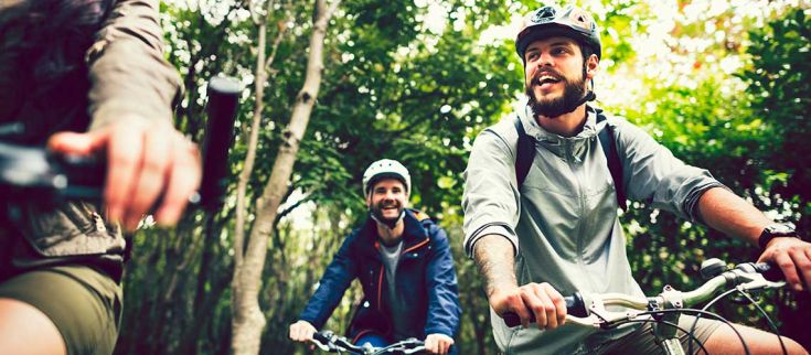 Due amici pedalano in un paesaggio naturale, sorridendo e apprezzando la campagna verde.