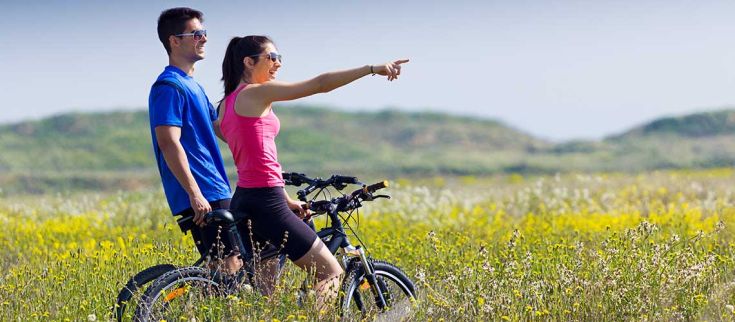 Due ciclisti sorridenti in un campo fiorito, apprezzando la tranquillità del luogo e condividendo un momento felice.
