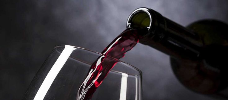 Un calice di vino rosso si riempie lentamente, catturando la luce in un gioco di riflessi. Ideale per un brindisi.