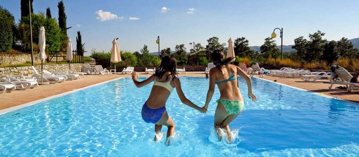 Due ragazze saltano con entusiasmo in una piscina trasparente mentre il sole splende.