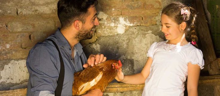 Un uomo e una ragazzina sorridono mentre accarezzano una gallina in un ambiente naturale.