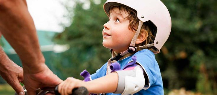 Un bambino con un casco sorride mentre gioca con una bicicletta, esprimendo felicità e voglia di divertirsi.