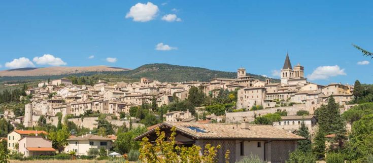 Una scena tranquilla di un borgo umbriano circondato da colline, con case in pietra e un panorama montano.
