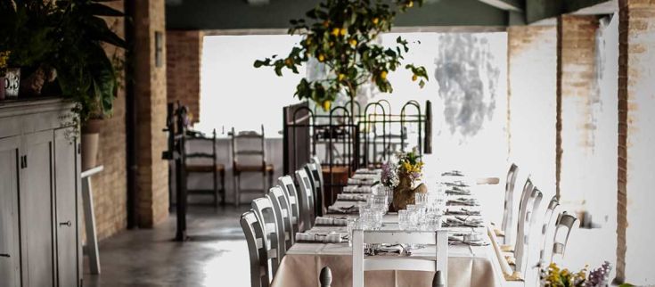 Interno di un ristorante con tavoli semplicemente apparecchiati e una pianta di limoni al centro, accogliente e invitante.