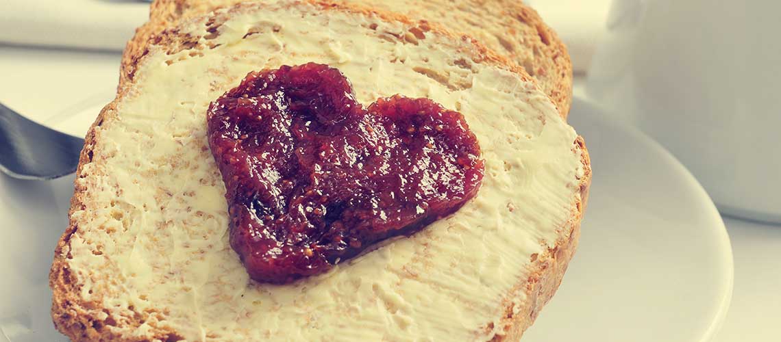 Una fetta di pane spalmata di burro con marmellata a forma di cuore, un'accogliente idea per una merenda.