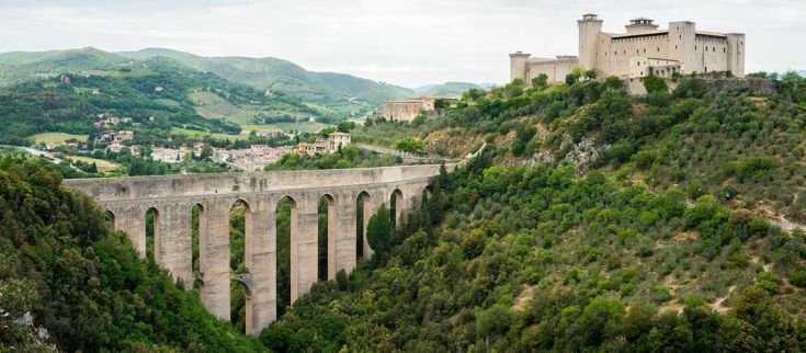 Un panorama di un antico ponte e di un palazzo, circondati da colline verdi.