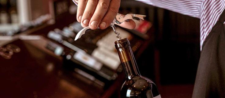 Un sommelier utilizza un cavatappi per aprire una bottiglia di vino in un ambiente tranquillo e raffinato.