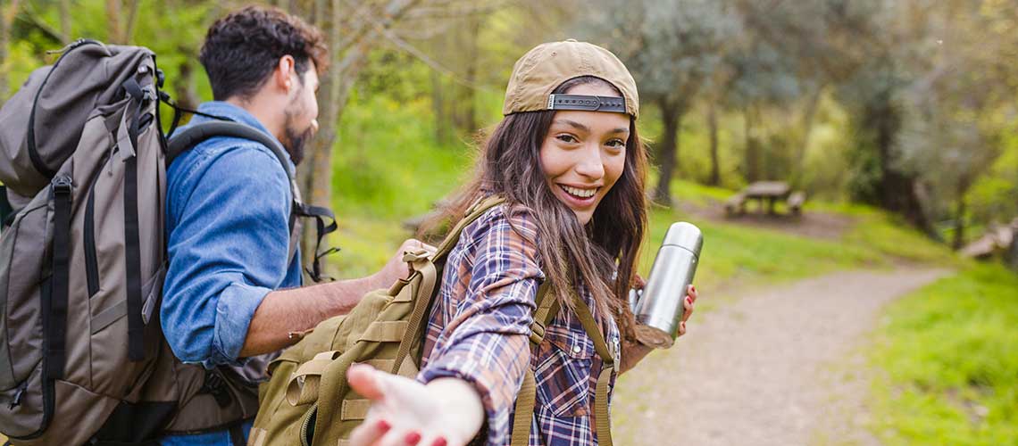 Due amici stanno facendo una passeggiata nel verde, sorridendo e godendo di momenti felici insieme. La ragazza porta una borraccia d'acqua.