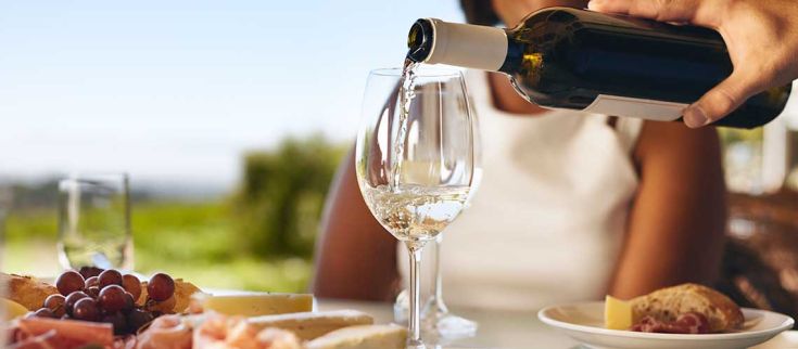 Un bicchiere di vino si trova accanto a un piatto di salumi e formaggi, immerso in un ambiente naturale.