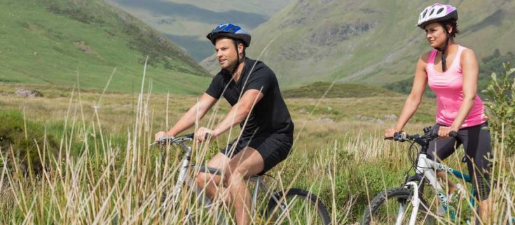 Due ciclisti si trovano in una zona verde, immersi nella natura, mentre pedalano lungo una strada tranquilla.