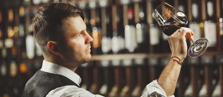 Un sommelier guarda attentamente un bicchiere di vino in un ambiente raffinato.