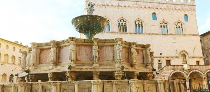 Una fontana storica situata in una piazza, circondata da elementi architettonici caratteristici del luogo.