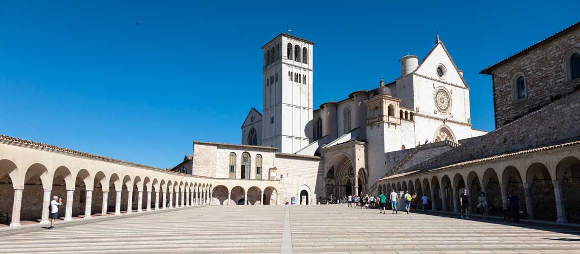 La Basilica di San Francesco ad Assisi in una giornata soleggiata, circondata da archi e visitatori.